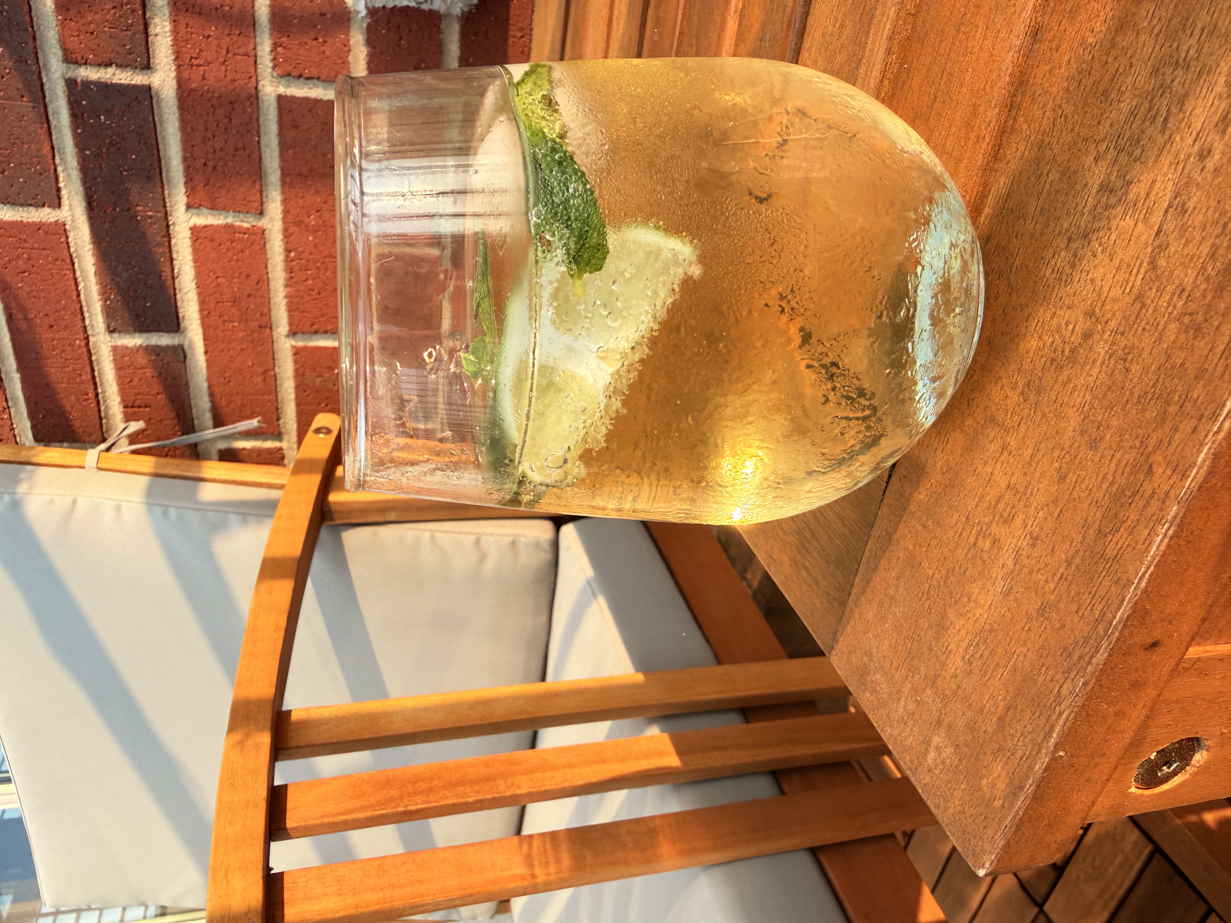 A Hugo Spritz cocktail tilted with mint and lime pressed against the glass, warm evening light shining through