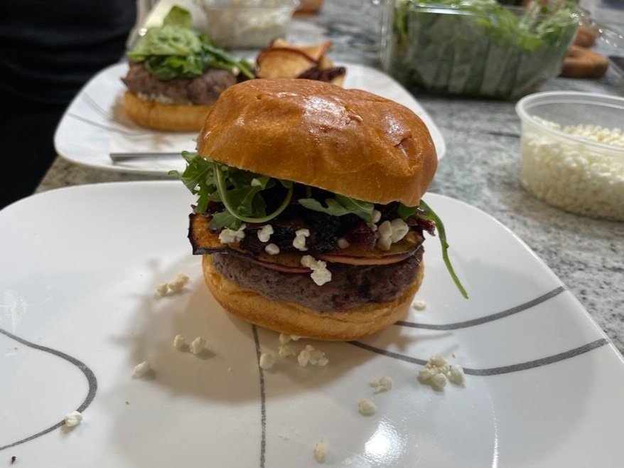 A close-up of the burger's toppings: candied apples, feta, and bourbon bacon jam piled high