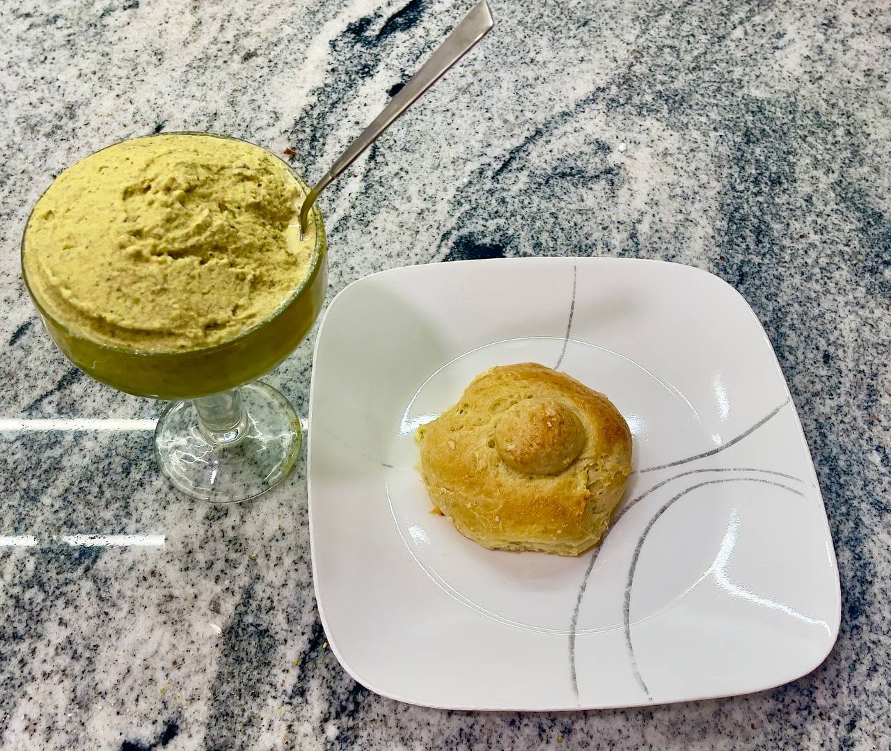 A plate of golden brioche con tuppo beside a glass of pistachio granita on a sun-drenched Sicilian morning