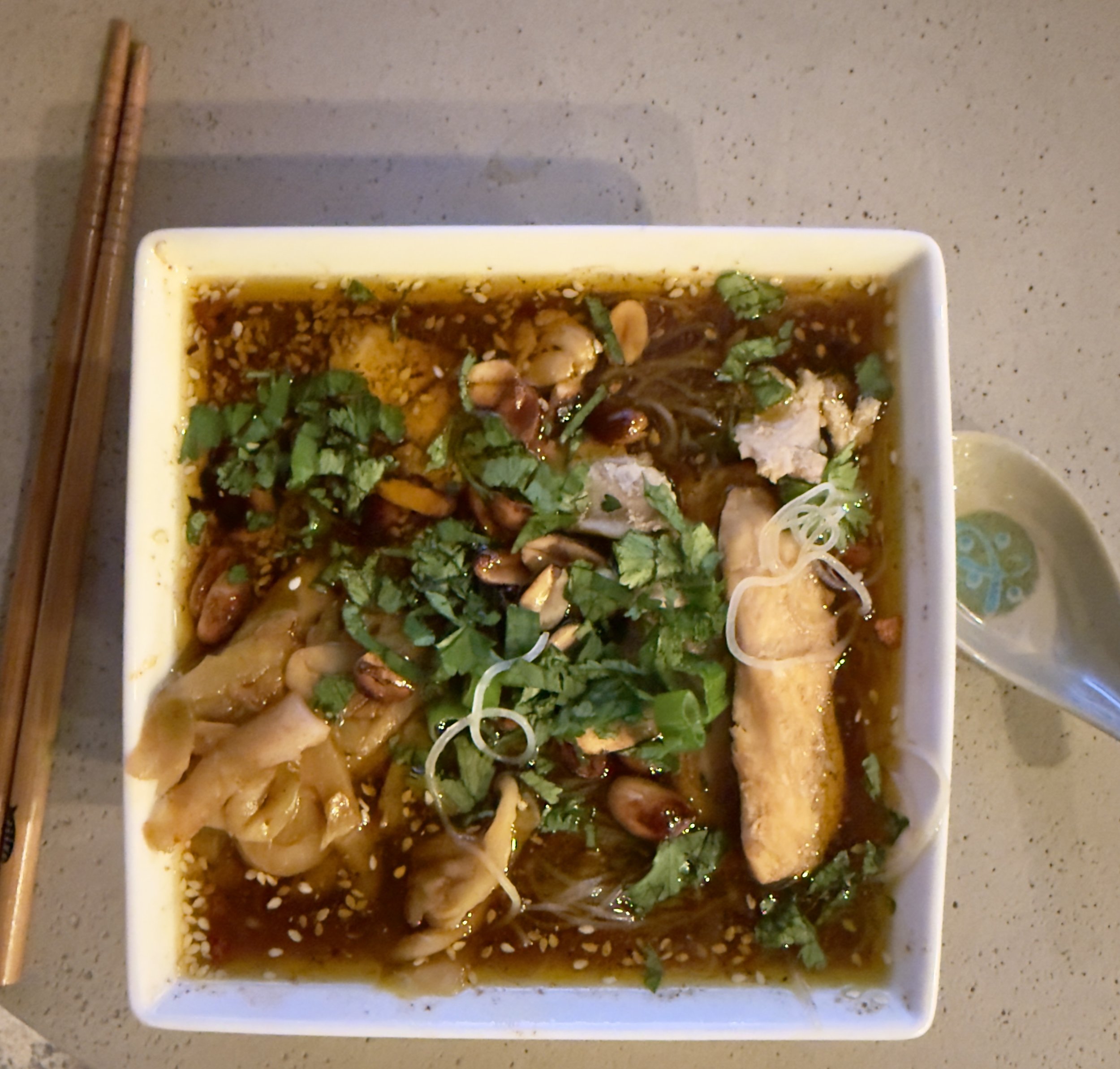A steaming bowl of Suan La Fen, hot and sour sweet potato glass noodle soup, garnished with peanuts and scallions