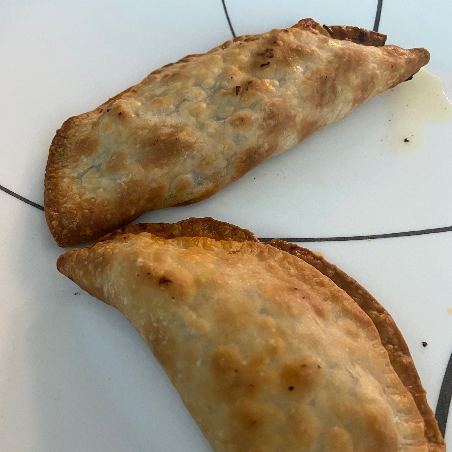 A plate of empanadas de pato served with a small bowl of aji amarillo dipping sauce