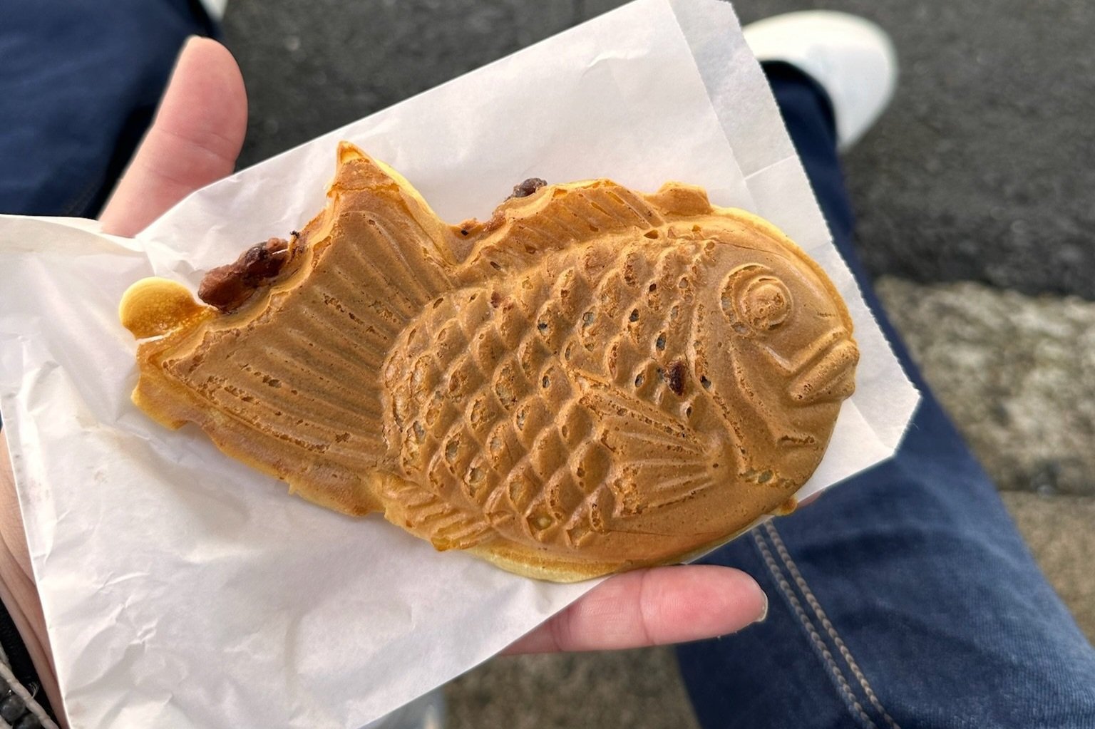 A vendor's hands pouring batter into fish-shaped taiyaki molds over a steaming griddle